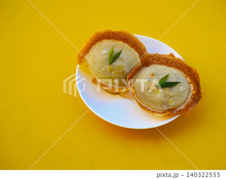Traditional Indonesian sweet snack Serabi or coconut milk pancakes garnished with a piece of pandan leaf, served on a white plate against a vibrant yellow background with copy space. Traditional Indonesian sweet snack Serabi or coconut milk pancakes garnished with a piece of pandan leaf, served on a white plate against a vibrant yellow background with copy space. 140322555
