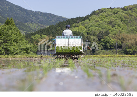 新緑の山並みと青空の下で田植え機を走らせる農家の作業風景 新緑の山並みと青空の下で田植え機を走らせる農家の作業風景 140322585