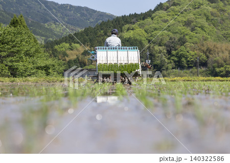 新緑の山々と青空のもと田植え機で苗を植える農家の風景 新緑の山々と青空のもと田植え機で苗を植える農家の風景 140322586