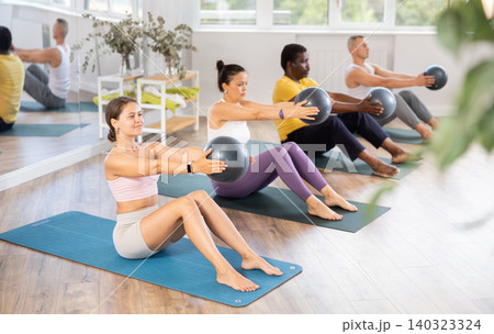 Young woman performing sit-up with bender ball at pilates class Young woman performing sit-up with bender ball at pilates class 140323324