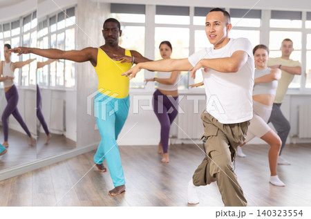 Positive man dancing and training movements Latin dance bachata during group class in choreography studio 140323554