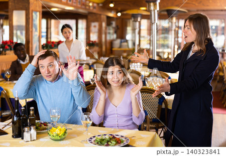 Resentful wife scolding her husband spending time with another woman at dinner Resentful wife scolding her husband spending time with another woman at dinner 140323841
