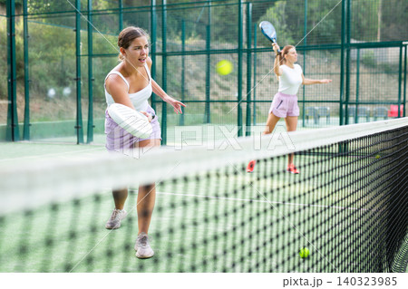 Female player playing padel in a padel court outdoor behind net 140323985