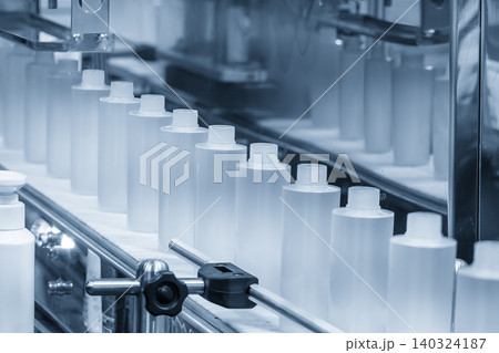 Row of liquid cosmetics bottles moving along a conveyor belt in an automated production line. 140324187