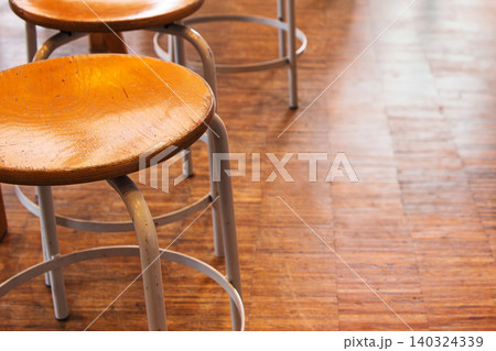 A row of round wooden stools with metal legs placed along a wooden floor in an empty classroom or art studio. Selective focus A row of round wooden stools with metal legs placed along a wooden floor in an empty classroom or art studio. Selective focus 140324339
