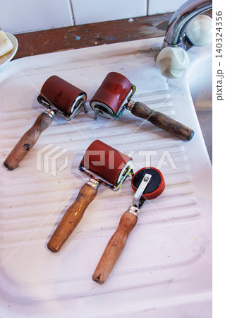 Cleaned printmaking brayer and ink roller tools with wooden handles resting on a white sink surface in the art studio after a linocut printing session. Selective focus Cleaned printmaking brayer and ink roller tools with wooden handles resting on a white sink surface in the art studio after a linocut printing session. Selective focus 140324356