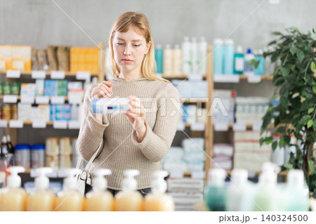 Young woman client choosing ointment in box in drugstore Young woman client choosing ointment in box in drugstore 140324500