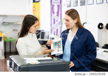 Two employees of printing house are discussing quality of plotter printing on color table 140324549