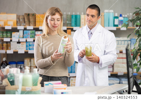 Young woman choosing shampoo while pharmacist offering in drugstore 140324553