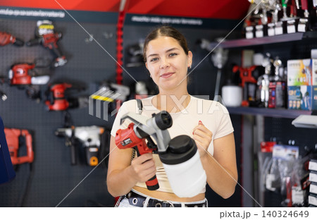 Woman choose examine handheld portable spray gun, airbrush in tools department of construction store 140324649