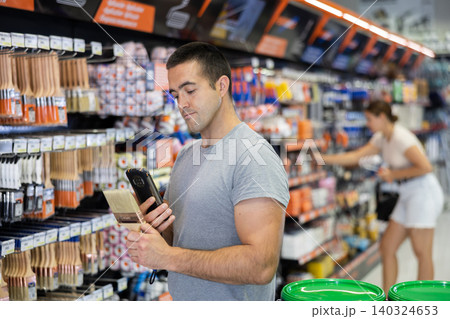 Man examines product in paint shop and scans QR code on label of brush for painting concrete walls 140324653