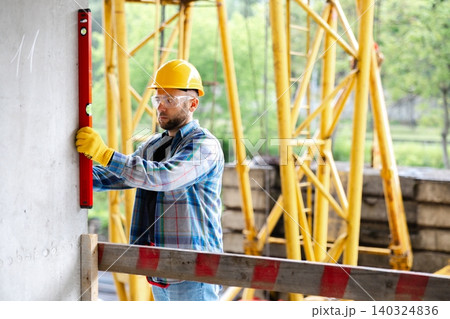 Construction worker checking wall level at building site Construction worker checking wall level at building site 140324836