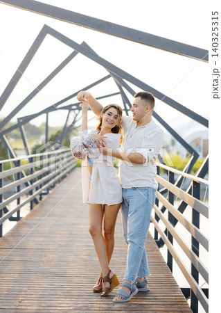A Romantic Couple Gracefully Dances on a Charming Wooden Bridge Beneath a Sturdy Metal Structure Overhead A Romantic Couple Gracefully Dances on a Charming Wooden Bridge Beneath a Sturdy Metal Structure Overhead 140325315