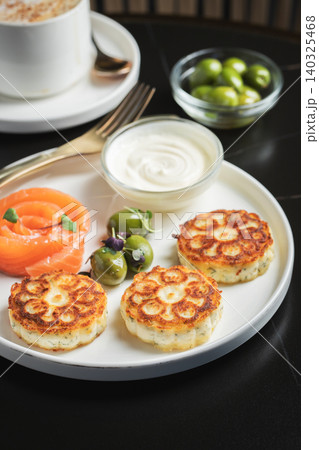 Savory Syrniki with Smoked Salmon, Olives and Sour Cream on White Plate Savory Syrniki with Smoked Salmon, Olives and Sour Cream on White Plate 140325468