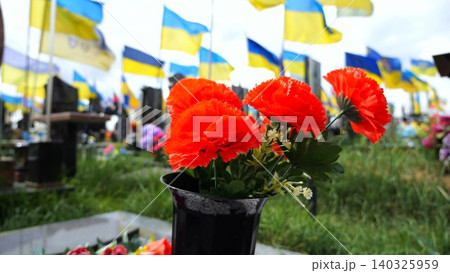 Bright red poppies flower serving as universal sign of memory in military cemetery. At blurred background ukrainian flags mark graves of fallen soldiers creating solemn tribute to sacrifice and memory Bright red poppies flower serving as universal sign of memory in military cemetery. At blurred background ukrainian flags mark graves of fallen soldiers creating solemn tribute to sacrifice and memory 140325959
