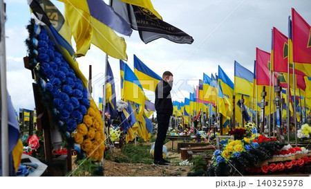 Mourning man standing among countless graves of ukrainian soldiers with national banners pay tribute to fallen family member in Kharkiv. Scene reflect personal sorrow loss caused by russian aggression Mourning man standing among countless graves of ukrainian soldiers with national banners pay tribute to fallen family member in Kharkiv. Scene reflect personal sorrow loss caused by russian aggression 140325978