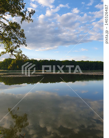 Picturesque summer landscape: mirror lake with reeds, reflection of clouds in the water, green forest on the horizon Picturesque summer landscape: mirror lake with reeds, reflection of clouds in the water, green forest on the horizon 140326487