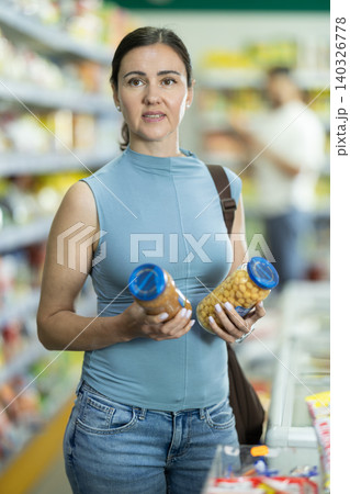 Middle-aged woman choosing canned goods in supermarket Middle-aged woman choosing canned goods in supermarket 140326778