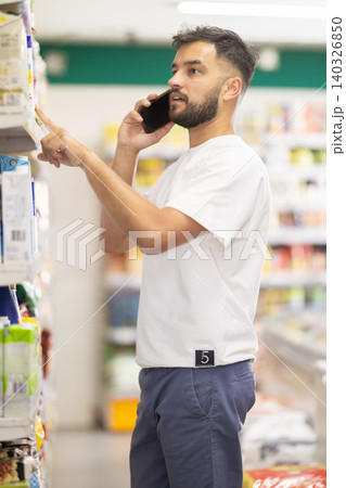 Man talks on phone and chooses baby formula and consults with his wife. Man talks on phone and chooses baby formula and consults with his wife. 140326850