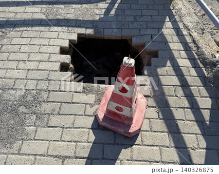 Traffic cone and hole on brick paved sidewalk, illustrating urban maintenance concept Traffic cone and hole on brick paved sidewalk, illustrating urban maintenance concept 140326875