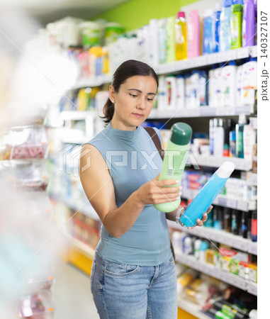 Woman examines product shampoo or shower gel in store Woman examines product shampoo or shower gel in store 140327107