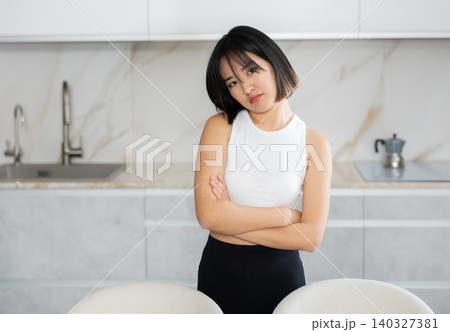 Sad young Asian girl standing at table in the kitchen Sad young Asian girl standing at table in the kitchen 140327381