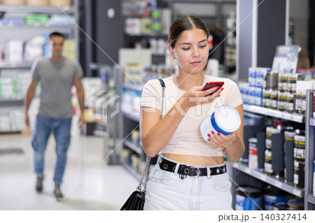 Woman examines product in paint shop and scans QR code on label of tin enamel dye Woman examines product in paint shop and scans QR code on label of tin enamel dye 140327414