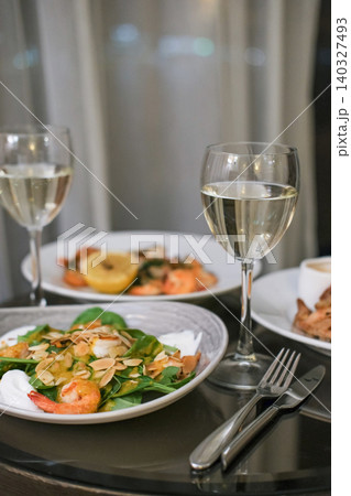 Elegant dinner for two featuring shrimp salads with almond flakes, lemon and glasses of white wine on dark reflective table in hotel room. Concept of luxury dining and romantic evening 140327493
