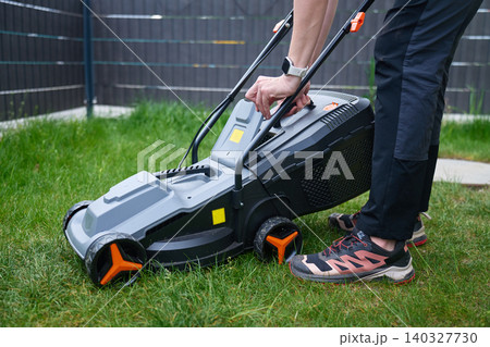 Person touches grass collector on lawn mower standing on backyard grass Person touches grass collector on lawn mower standing on backyard grass 140327730