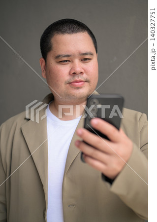 Focused plus size Isan Thai businessman using phone near grey wall vertical Focused plus size Isan Thai businessman using phone near grey wall vertical 140327751