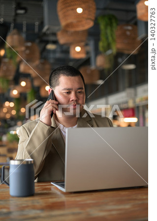 Pensive plus size Isan Thai businessman on phone call with laptop vertical 140327763