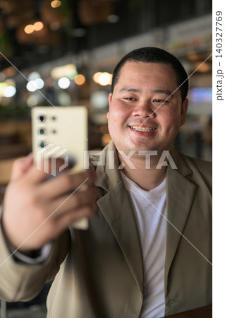 Happy plus size Isan Thai businessman taking selfie at cafe vertical Happy plus size Isan Thai businessman taking selfie at cafe vertical 140327769