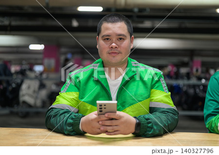 Thai delivery man from Isan looking at camera holding smartphone inside garage Thai delivery man from Isan looking at camera holding smartphone inside garage 140327796