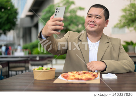 Happy plus size Isan Thai businessman taking selfie with pizza outdoors 140327820
