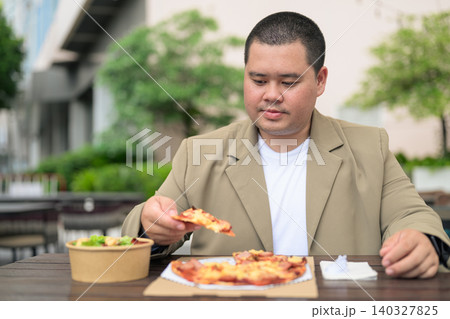 Plus size Isan Thai businessman eating pizza at outdoor cafe 140327825