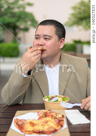 Plus size Isan Thai man eating pizza slice at outdoor restaurant vertical 140327835