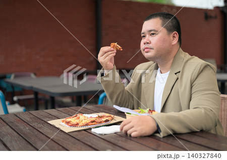 Pensive plus size Isan Thai businessman with pizza slice outdoors 140327840