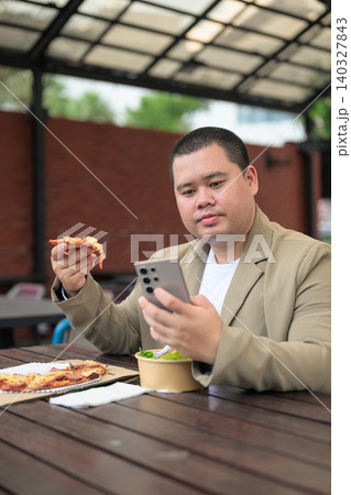 Focused plus size Isan Thai businessman with phone and pizza vertical 140327843