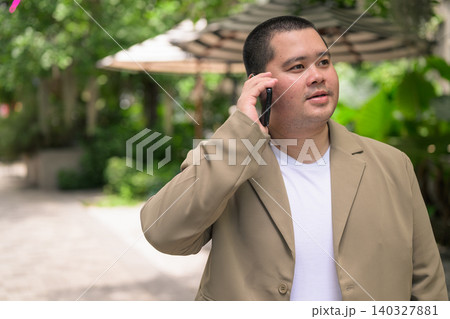 Pensive plus size Isan Thai businessman calling on phone in garden Pensive plus size Isan Thai businessman calling on phone in garden 140327881