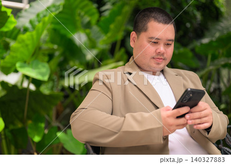 Focused plus size Isan Thai businessman using phone in garden 140327883