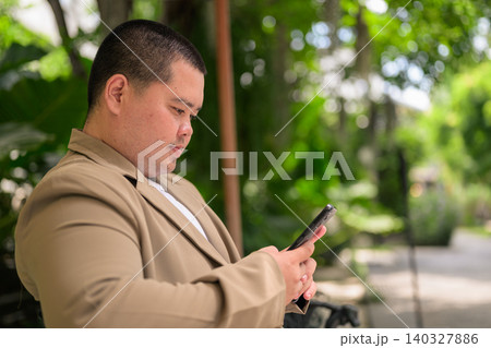 Profile of plus size Isan Thai businessman using phone in garden 140327886