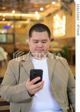 Focused plus size Isan Thai businessman reading smartphone at restaurant vertical 140327915