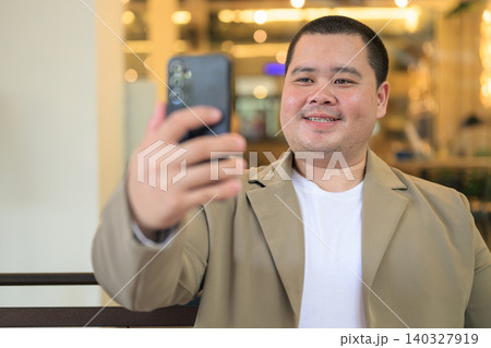 Smiling plus size Isan Thai businessman taking selfie at restaurant Smiling plus size Isan Thai businessman taking selfie at restaurant 140327919