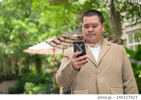 Focused plus size Isan Thai businessman using phone in garden 140327923