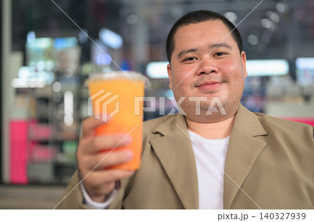 Confident plus size Isan Thai man offering orange juice at night cafe 140327939