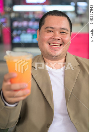 Happy plus size Isan Thai man offering orange juice vertical shot Happy plus size Isan Thai man offering orange juice vertical shot 140327942