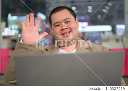 Cheerful plus size Isan Thai businessman waving at laptop video call horizontal shot 140327969