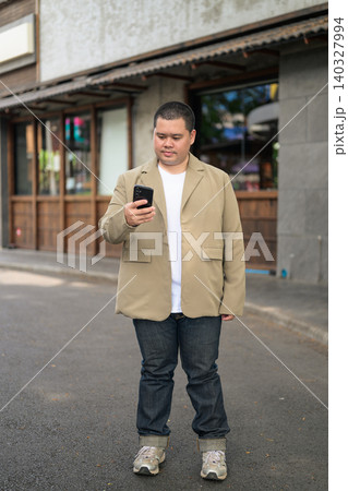 Plus size Isan Thai businessman using phone on an urban street Plus size Isan Thai businessman using phone on an urban street 140327994