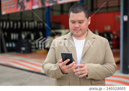 Plus size Isan Thai businessman using phone at a car service center 140328005