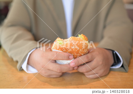 Close up of a plus size Thai man holding a bitten hamburger at a table 140328018